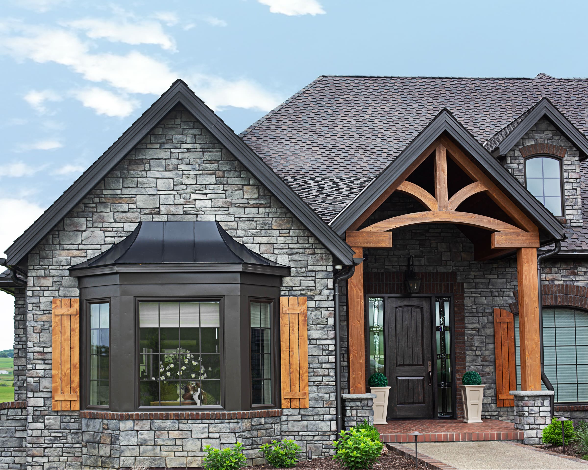 A luxurious home’s exterior featuring timber framing for the porch and black trim.